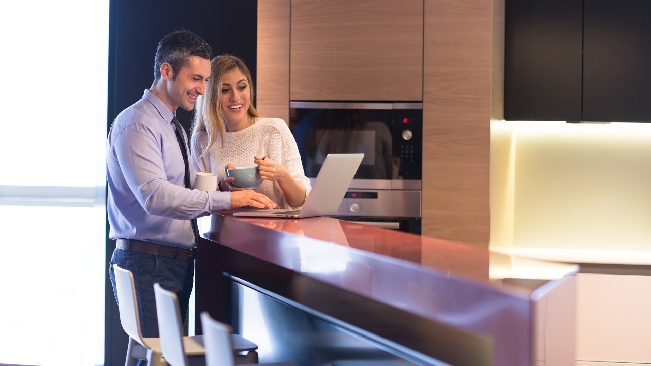 Happy couple using laptop in the kitchen; image used for the HSBC International Services Employee Banking Solutions Page.