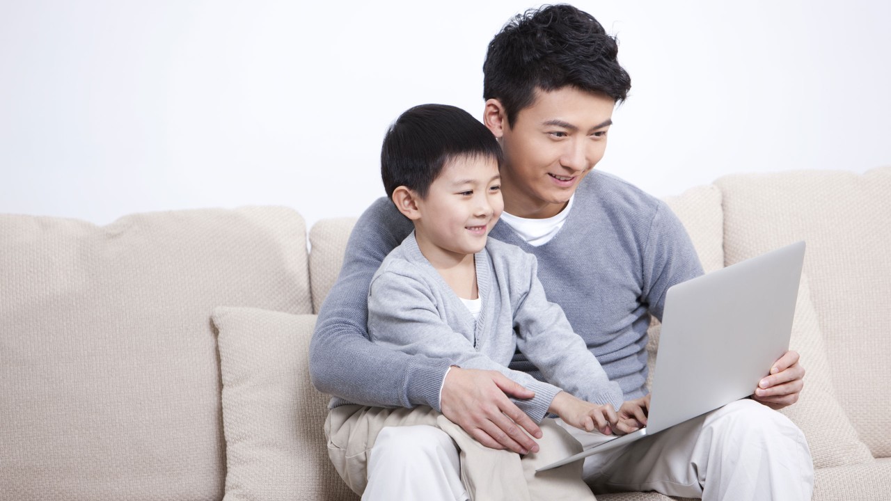 Man and young son sitting on sofa with laptop; Image use for image used for HSBC International Services life abroad article Basics of paying taxes.