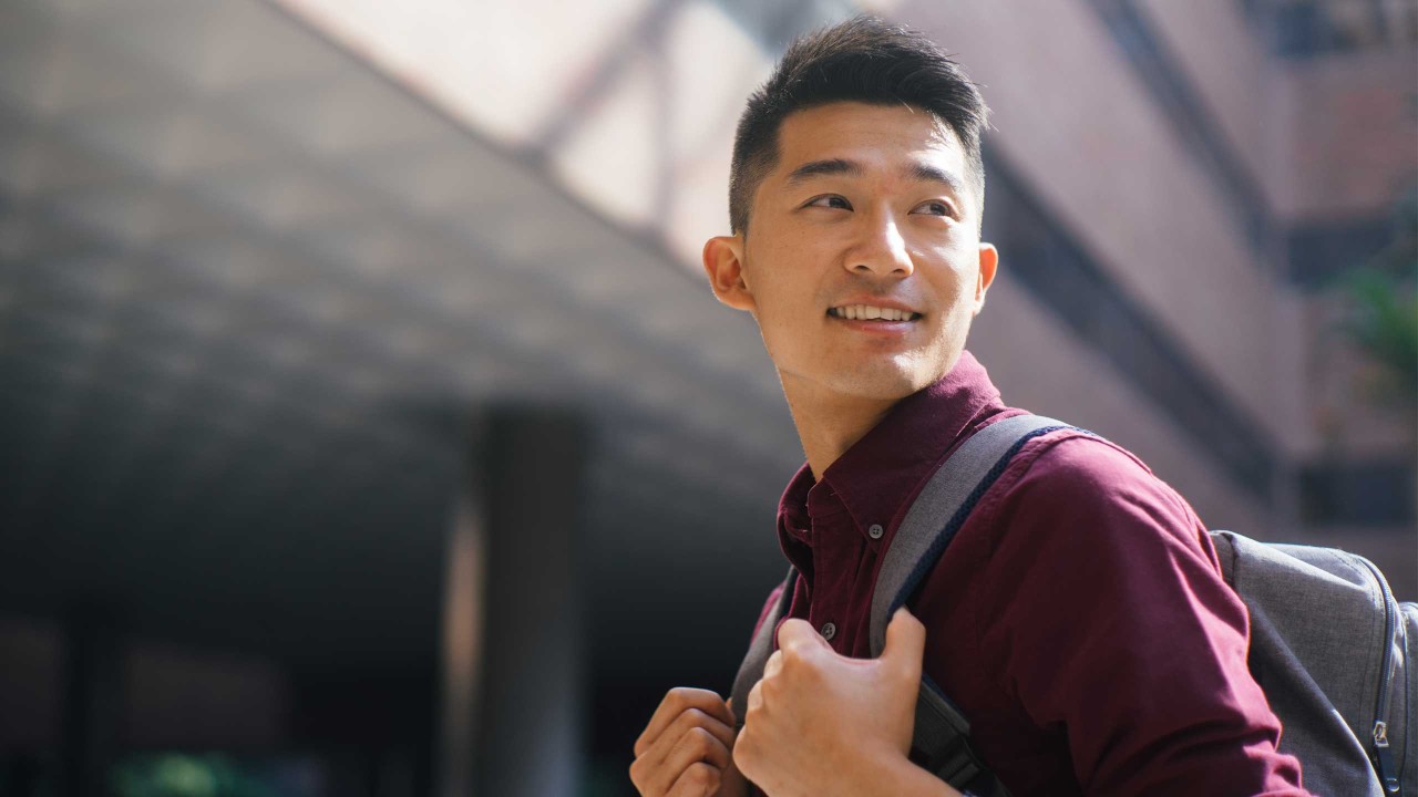 Young man with backpack, looking over his shoulder and smiling; image used for HSBC International Services Study Abroad graduate choices..